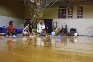 Girls roll balls across gym floor