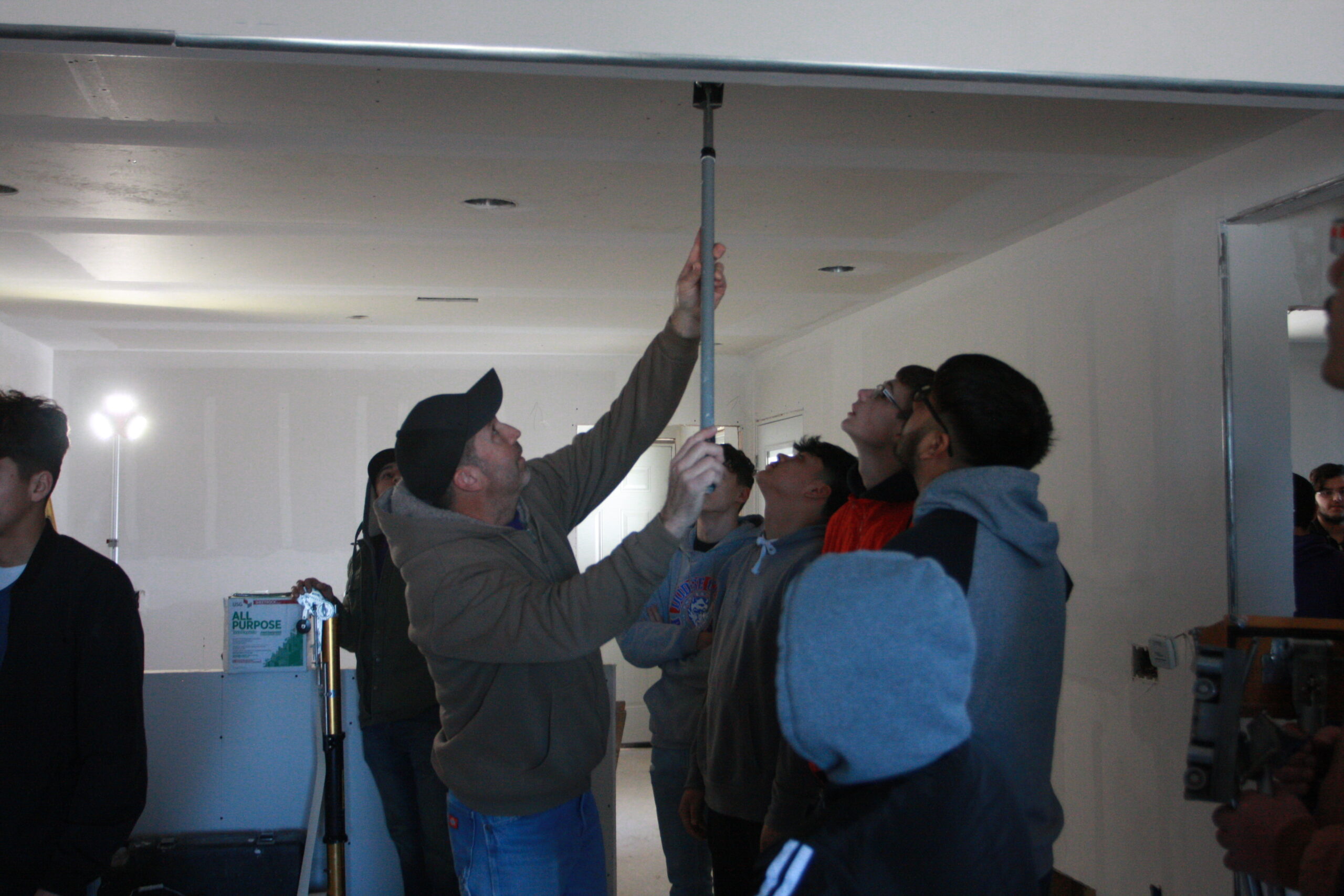 Professor Pat Shiew demonstrating a drywall tool during the CHAD house site visit during construction day